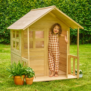 Une enfant se tient à l’entrée de la maisonnette en bois.