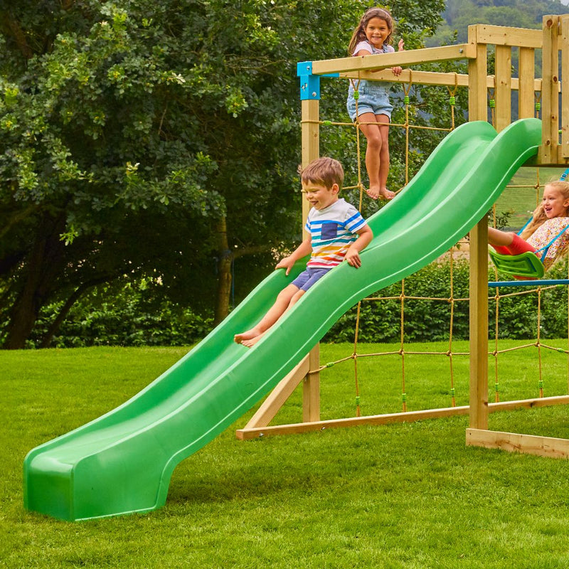 Trois enfants jouent sur une aire de jeux en bois avec un grand toboggan vert, un filet à grimper et une balançoire.