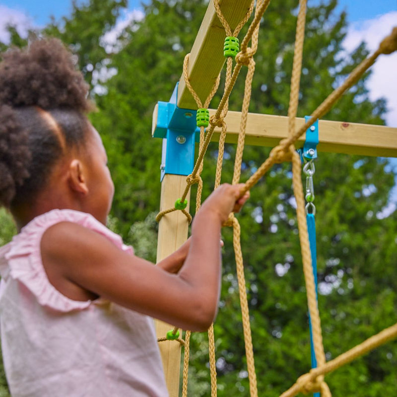 Enfant en train de grimper sur un filet fixé à une structure de jeux en bois, en extérieur.