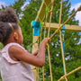 Enfant en train de grimper sur un filet fixé à une structure de jeux en bois, en extérieur.