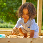 Un enfant joue dans un bac à sable en extérieur, tenant du sable dans ses mains.