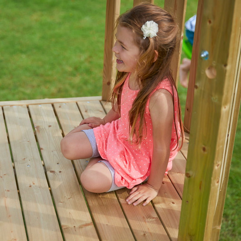Une enfant est assise en haut de l'aire de jeux en bois.
