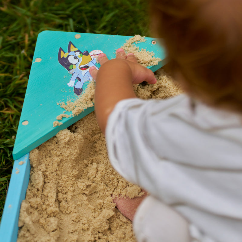Un enfant joue avec le sable dans le bac à sable Bluey.