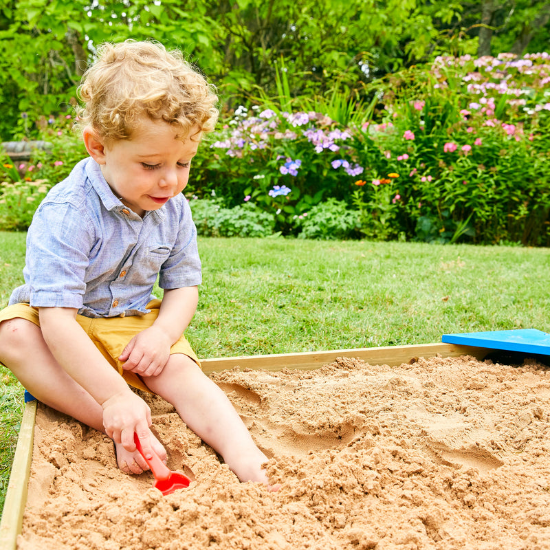 Un enfant joue dans un bac à sable, manipulant le sable avec un accessoire.