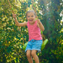Une enfant se balance sur une balançoire verte suspendue par des cordes, dans un jardin.