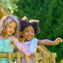 Deux enfants souriants jouant ensemble sur le balcon d’une cabane en bois pour jardin.