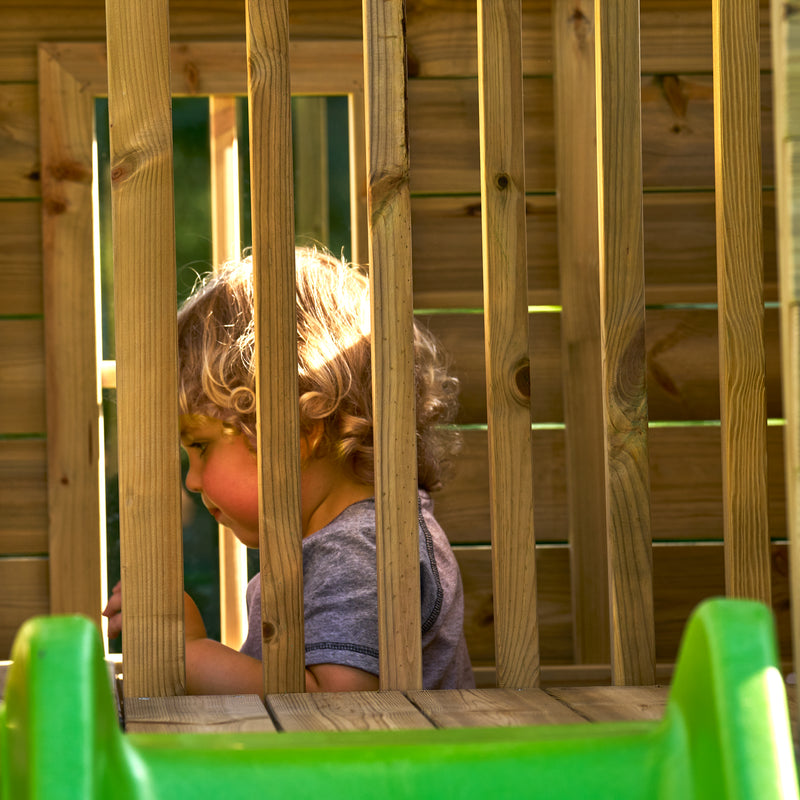 Enfant jouant à l'étage d'une maisonnette en bois.