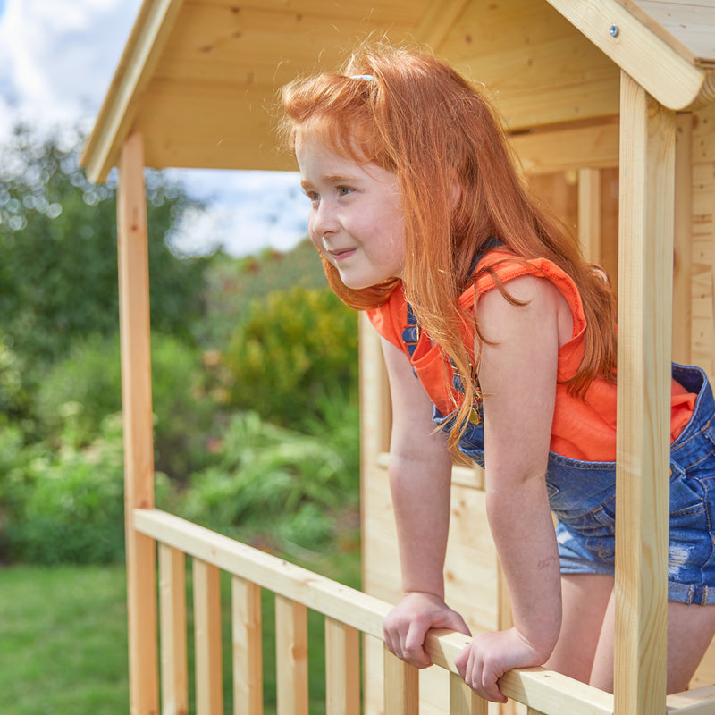 Une enfant se tient sur le balcon d’une cabane en bois sur pilotis.