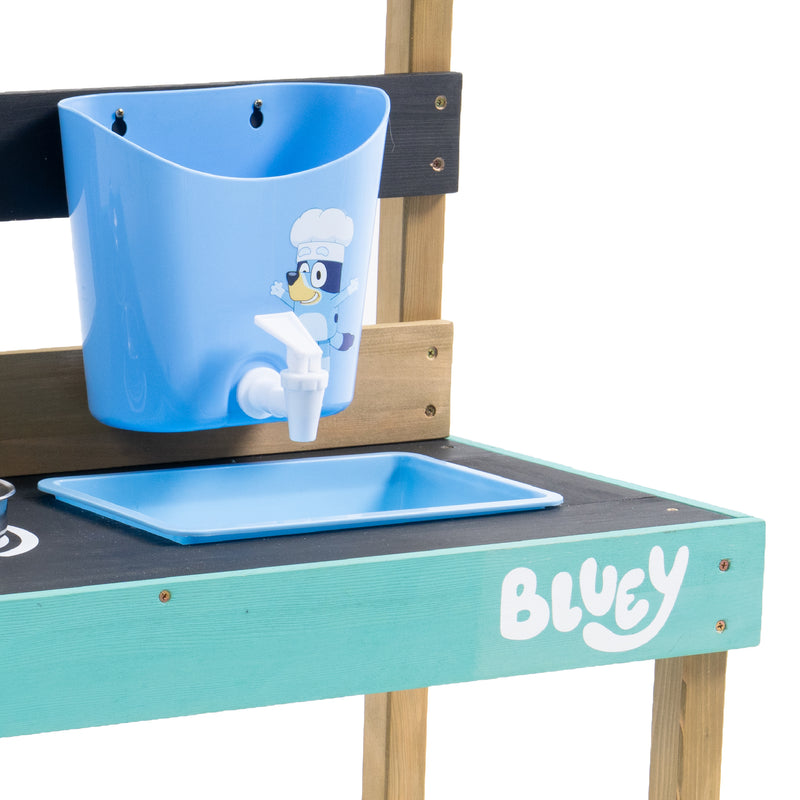 Détail de la cuisine d’extérieur pour enfant : réservoir d’eau bleu avec robinet blanc fixé au panneau arrière, bac de récupération et plan de travail turquoise décoré du logo Bluey.