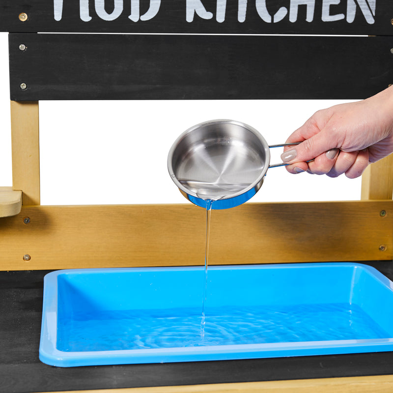 Un adulte verse de l’eau d’une casserole dans l’évier amovible de la cuisine en bois pour enfants.