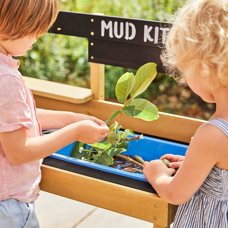 Des enfants jouent avec des feuilles et des branches dans l’évier amovible de la cuisine en bois pour enfants.