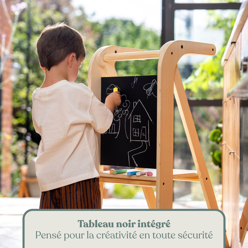 Enfant dessinant à la craie sur le tableau noir intégré de la tour d'apprentissage en bois