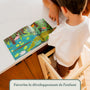 Vue du dessus d'un enfant sur la tour d'observation en bois, découvrant un livre illustré au plan de travail pour son éveil