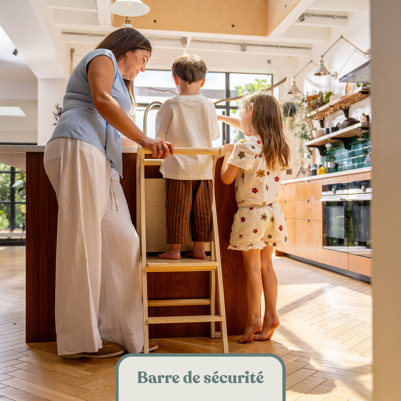 Enfant debout sur la tour d'apprentissage en bois avec barre de sécurité, en famille au plan de travail de la cuisine
