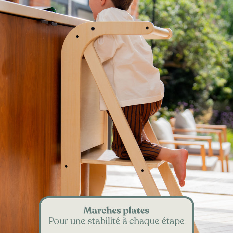 Enfant montant sur les marches plates de la tour d'apprentissage en bois pour atteindre le plan de travail de la cuisine