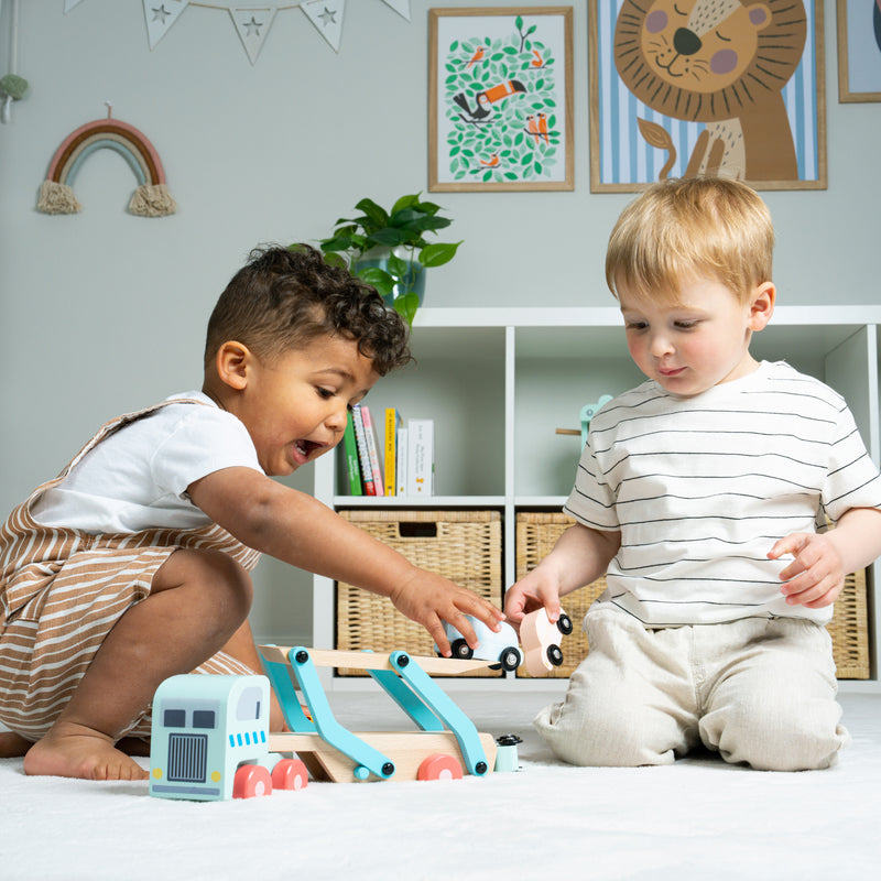 Deux enfants tiennent chacun une petite voiture et jouent avec un camion transporteur de voitures.
