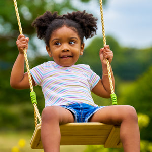 Une enfant est assise sur la balançoire en bois.