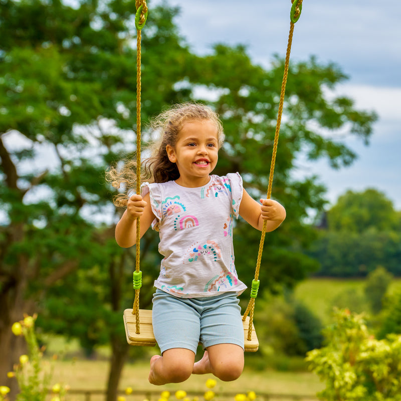 Une enfant est assise sur la balançoire en bois.