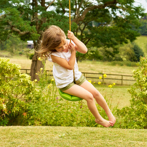 Une enfant se balance sur la balançoire ronde TP Toys en plastique rotomoulé haute densité.