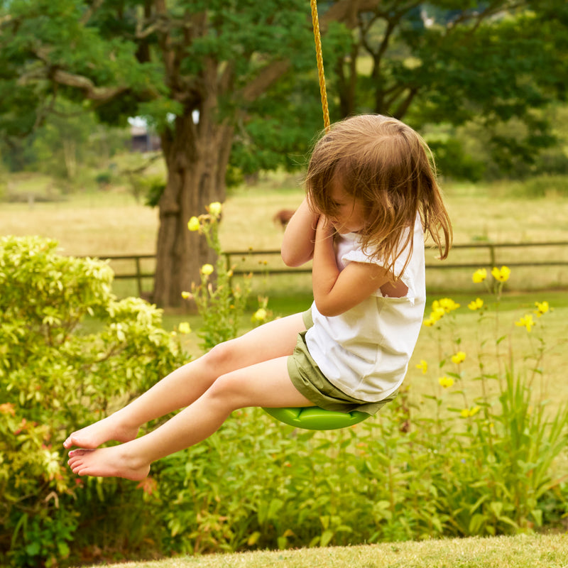 Une enfant se balance sur la balançoire ronde TP Toys en plastique rotomoulé haute densité.