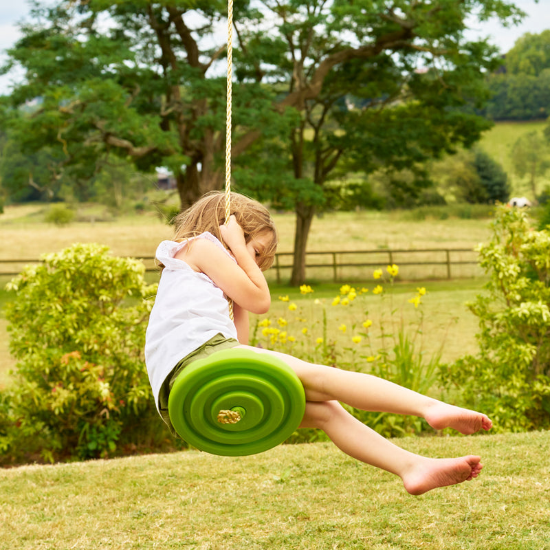 Une enfant se balance sur la balançoire ronde TP Toys en plastique rotomoulé haute densité.