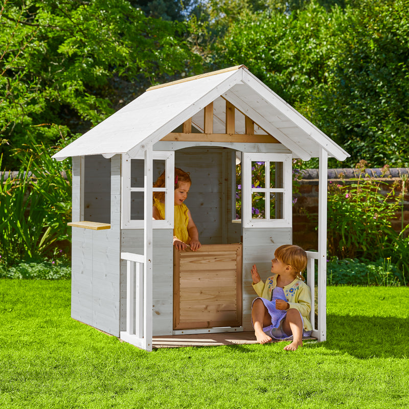 Une enfant est dans la maisonnette en bois dans le jardin, tandis qu’une autre enfant est assise devant.