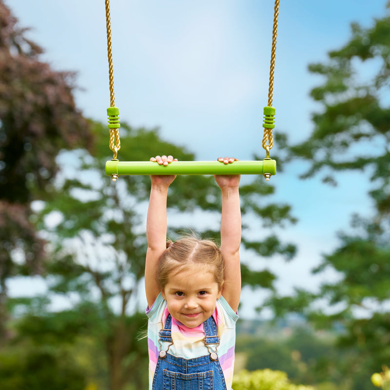 Une enfant se suspend au trapèze en métal TP Toys, conçu pour développer coordination, force et équilibre.