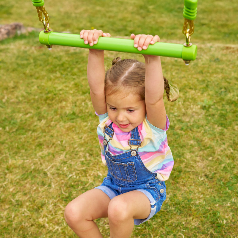 Une enfant se suspend au trapèze en métal TP Toys, conçu pour développer coordination, force et équilibre.
