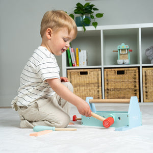 Enfant jouant avec la boîte à outils en bois, manipulant le marteau.