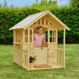 Une enfant joue dans une maisonnette en bois installée dans un jardin.