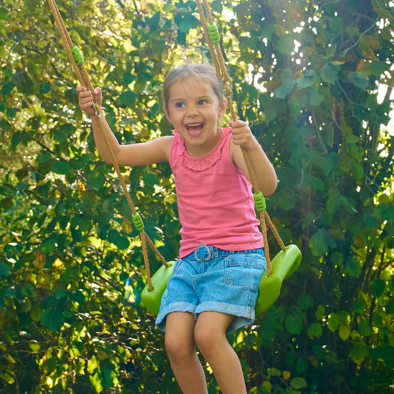 Une enfant se balance sur une balançoire verte suspendue par des cordes, dans un jardin.