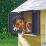 Enfant regardant par la fenêtre ouverte d’une maisonnette en bois, avec volets gris anthracite, dans un jardin.