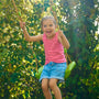 Une enfant se balance sur une balançoire verte suspendue par des cordes, dans un jardin.