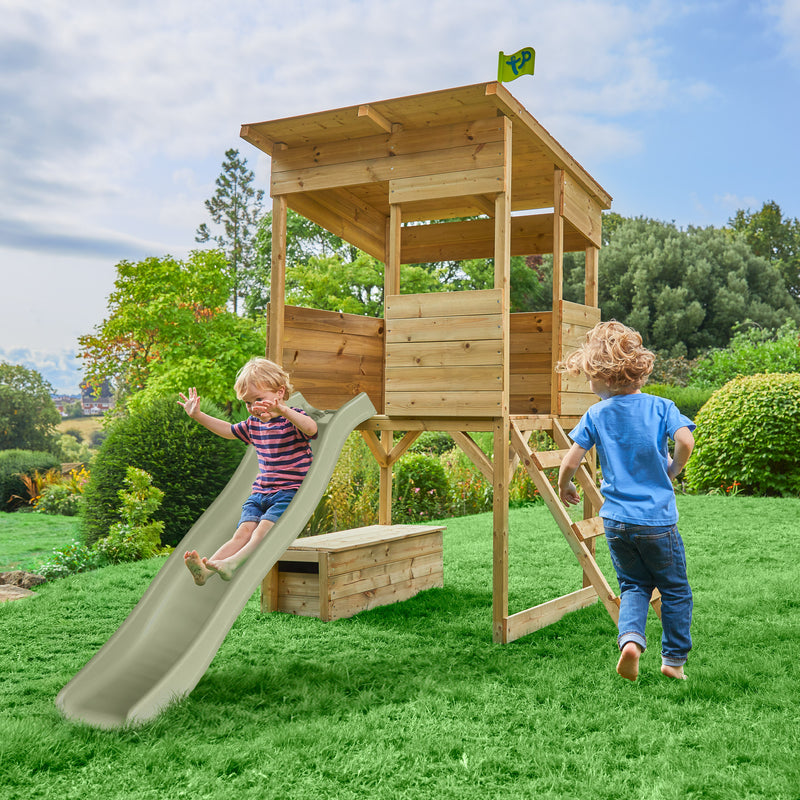 Maisonnette cabane sur pilotis en bois avec toboggan dans un jardin : un enfant glisse sur le toboggan tandis qu’un autre court vers l’échelle de la maisonnette.