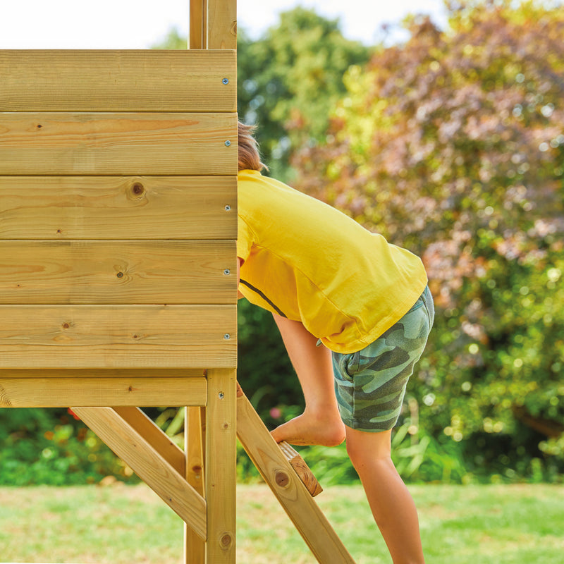 Un enfant grimpe par l’échelle de la maisonnette cabane en bois.
