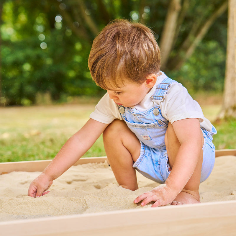 Jeune enfant jouant dans un bac à sable en bois installé dans un jardin.