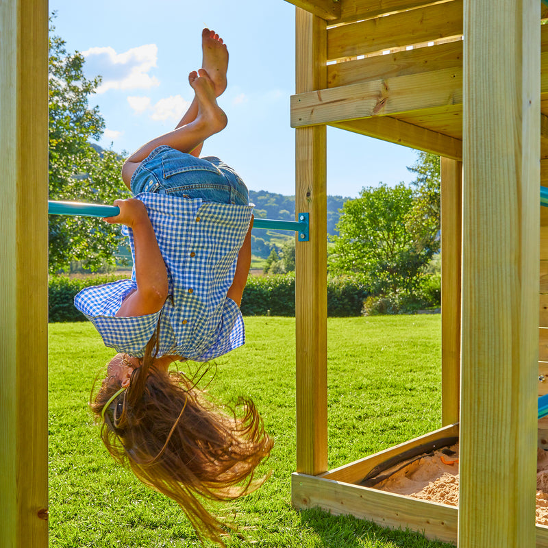 Une enfant se suspend à la barre en métal fixée sur la plateforme en bois.