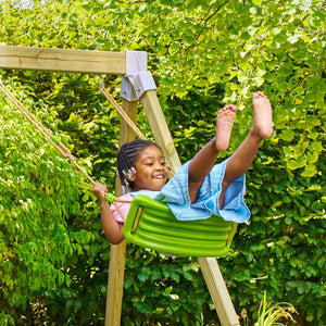 Une enfant se balance sur une balançoire verte suspendue par des cordes, dans un jardin.