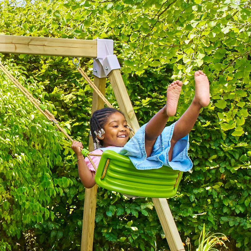 Une enfant se balance sur une balançoire verte suspendue par des cordes, dans un jardin.
