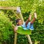 Une enfant se balance sur une balançoire verte suspendue par des cordes, dans un jardin.