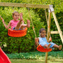 Deux enfants se balancent sur une balançoire rouge suspendue par des cordes, dans un jardin.