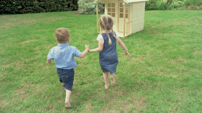 Des enfants jouent dans une maisonnette avec une cuisine extérieure, ils utilisent de petits ustensiles pour préparer des plats