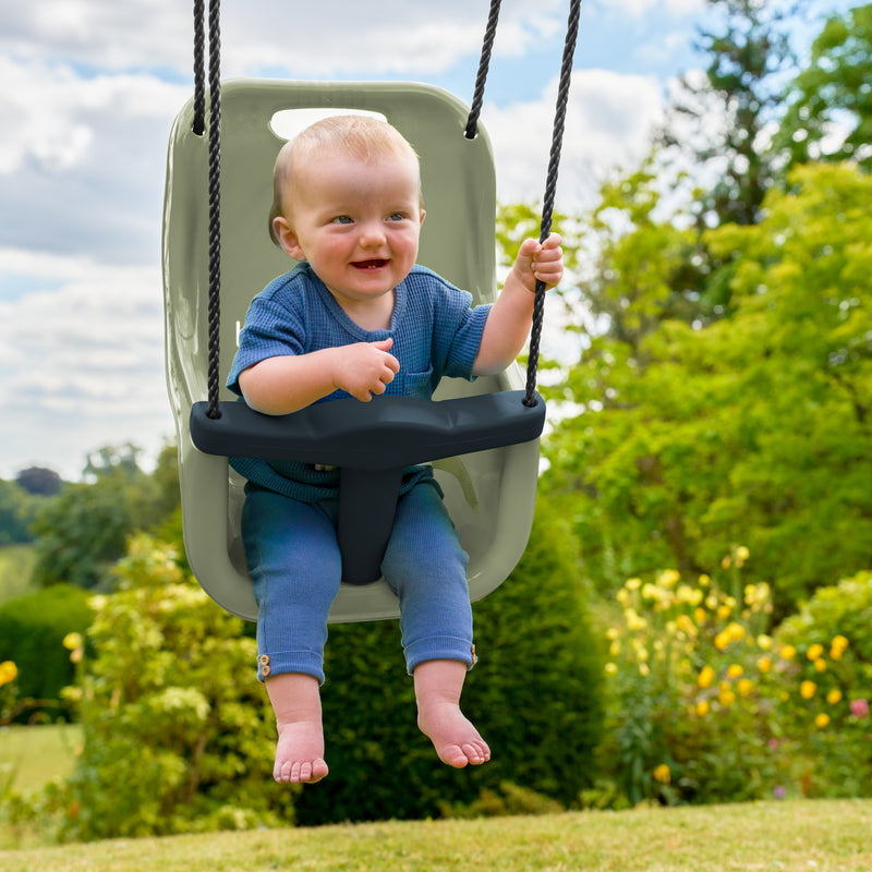 Un enfant est assis dans le siège bébé avec harnais 3 points, fixé à un portique de jeu.