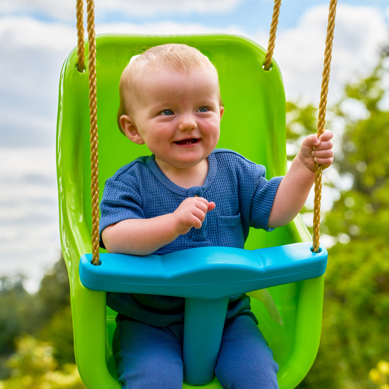 Un enfant est assis dans le siège bébé avec harnais 3 points, fixé à un portique de jeu.