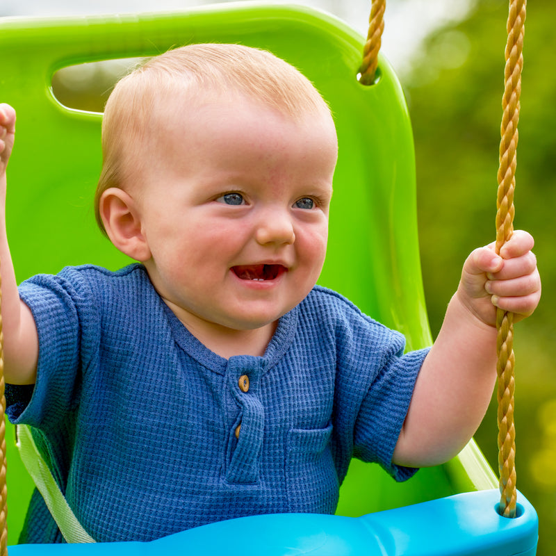Un enfant est assis dans le siège bébé avec harnais 3 points, fixé à un portique de jeu.