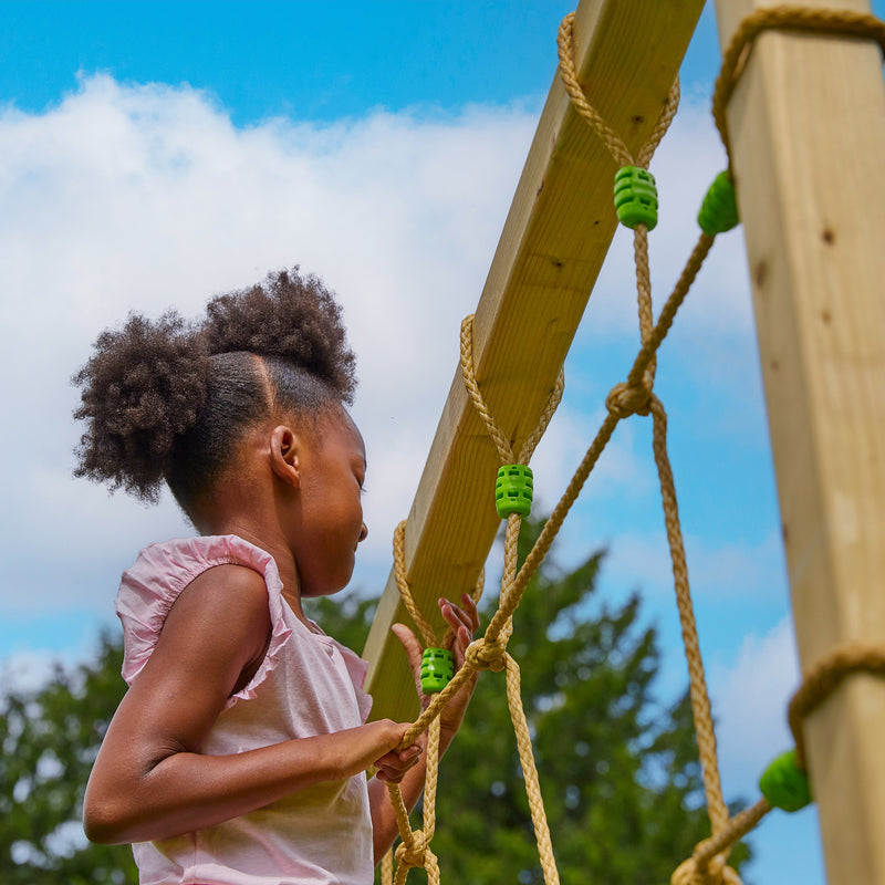 Une enfant développe sa motricité en grimpant le filet d’escalade.