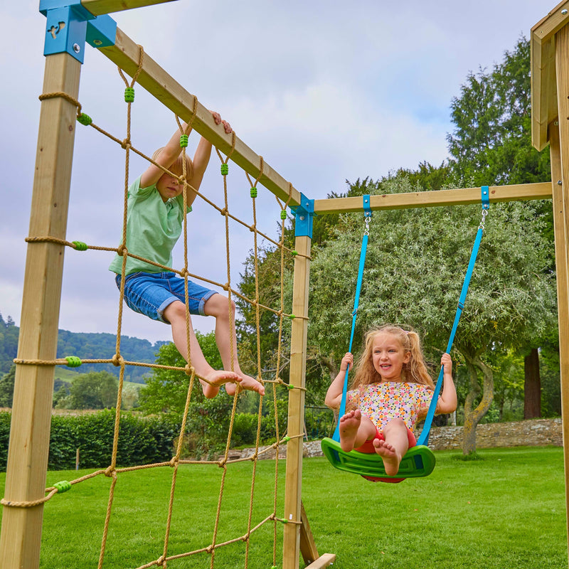 Un enfant grimpe le filet d’escalade Skywood pendant qu’une autre se balance sur la balançoire.