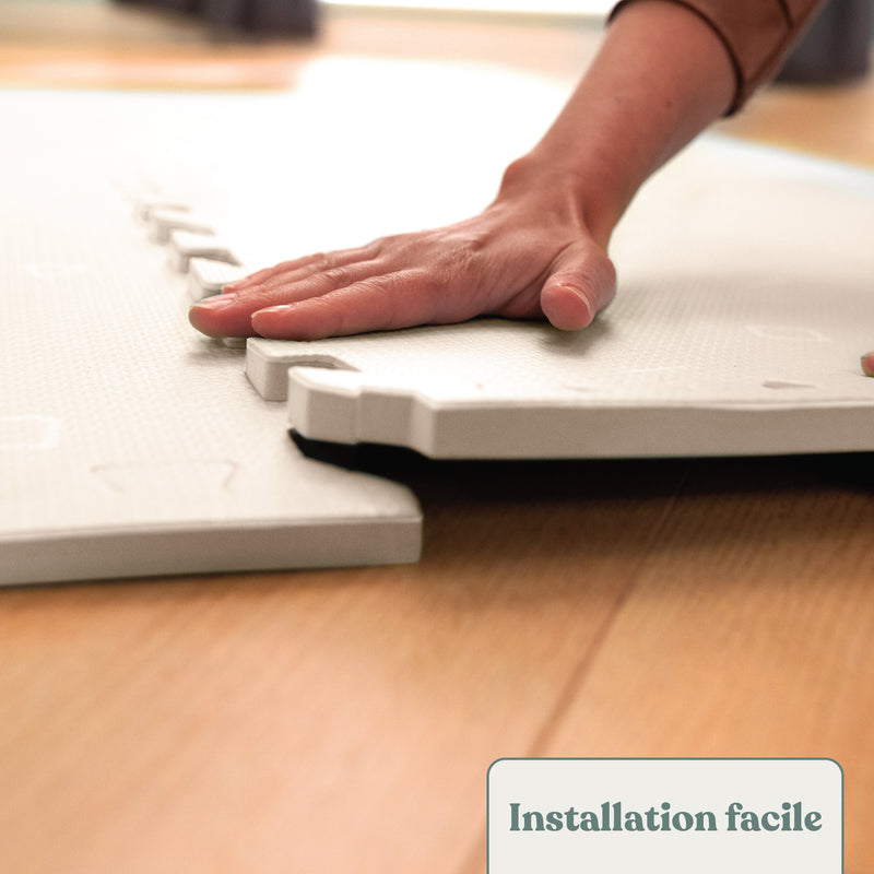 Une main emboite deux dalles de tapis mousse ensemble