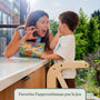 Enfant sur la tour d'apprentissage Montessori en bois, lisant un livre avec sa maman au plan de travail