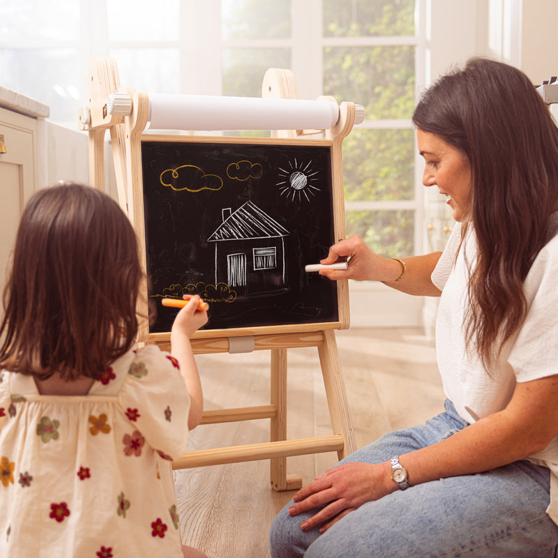 Une adulte dessine avec une enfant sur le tableau créatif intégré à la tour d’apprentissage.